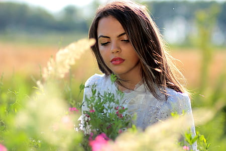 woman standing and looking at pink petaled flower thumbnail