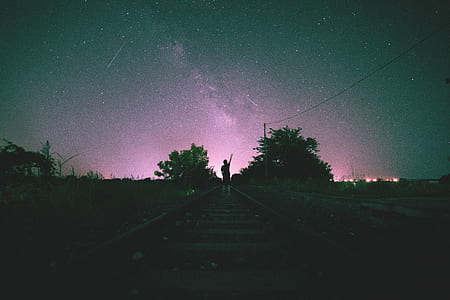 silhouette of man standing on train tracks during nighttime thumbnail