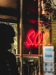 turned-on S.O.S. neon signage reflecting on glass thumbnail