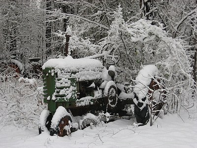 green tractor covered with snow surrounded by trees thumbnail