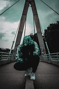 man wearing white and gray floral hooded jacket crouching on gray bridge thumbnail