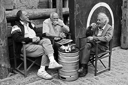 grayscale photography of three men sitting on chair while talking to each other thumbnail