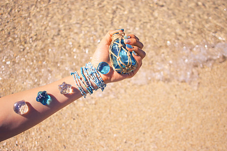 person holding translucent blue glass bottle with assorted accessories on his arm thumbnail