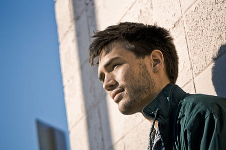man leaning on white concrete wall outside thumbnail