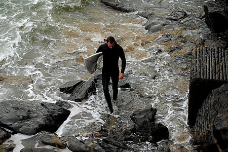 man wearing wet suit carrying surfboard thumbnail