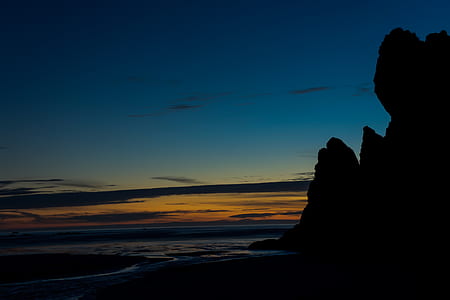silhouette photo of rock formation near body of water thumbnail
