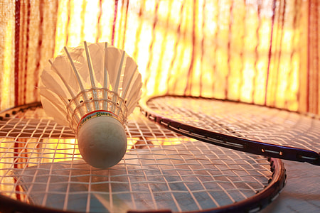 white shuttlecock on two black badminton rackets thumbnail