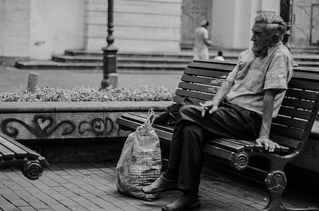 grayscale photo of old man sitting on bench thumbnail