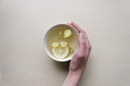 person holding white ceramic cup with sliced ginger and lemon thumbnail