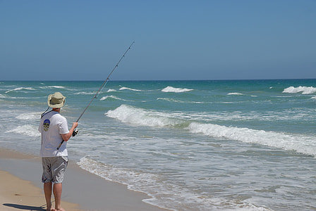 person standing near body of water holding fishing rod thumbnail