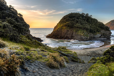 islet covered with green leafed trees in middle of ocean water surrounded by mountains during daytime thumbnail