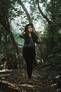 black haired woman in black top and pants walking in forest thumbnail