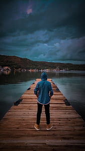 Man Wearing Blue Hoodie Standing On Wooden Dock thumbnail