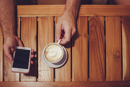 Person Holding Turned Off Gold Iphone 6 With Case and White Ceramic Cup Filled With Latte thumbnail