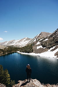 person standing on cliff facing body of water thumbnail