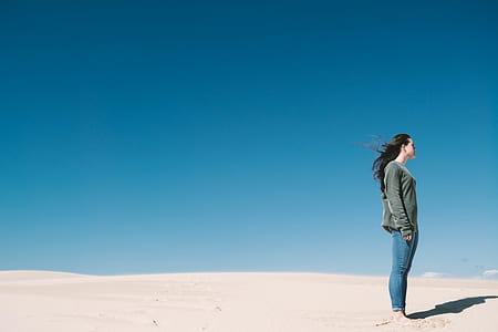 woman wearing gray sweatshirt and blue jeans standing on brown sand thumbnail
