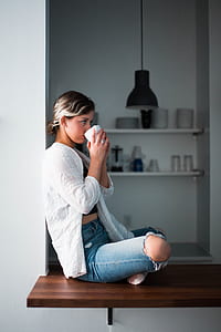 woman sitting on brown wooden platform sipping on white ceramic cup thumbnail