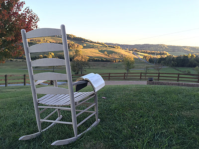 empty white wooden rocking chair with open book on green grass field thumbnail
