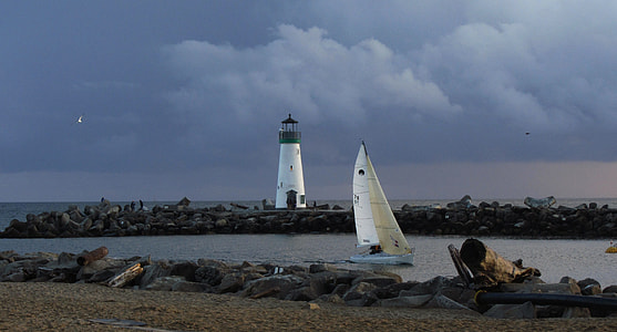 white sailing boat on body of water near black and white lighthouse thumbnail
