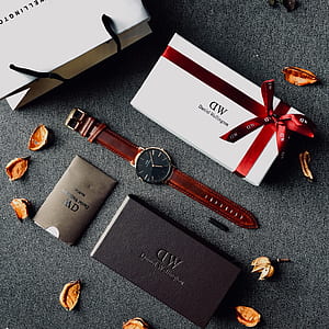 round black analog watch with brown leather strap beside white box thumbnail
