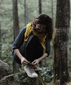 woman sitting on rock while lacing her shoes surrounded by trees thumbnail