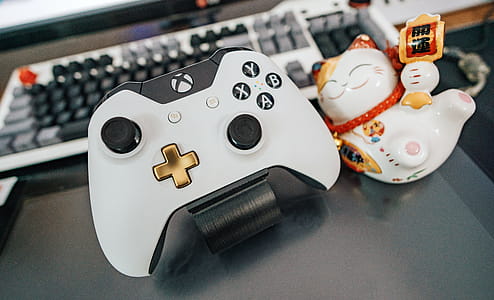 White and Black Xbox One Wireless Controller Beside White and Multicolored Ceramic Cat Figurine on Black Surface thumbnail
