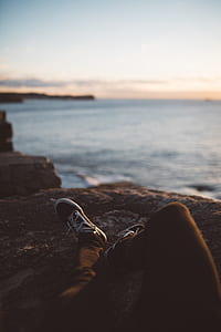 person sitting on brown rock in front of seashore thumbnail