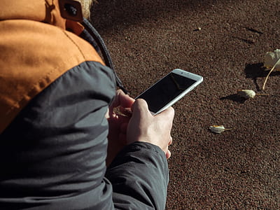 person in black jacket using white smartphone outdoors thumbnail