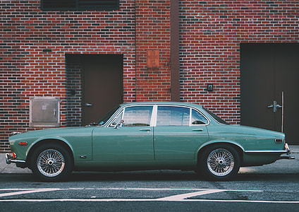 classic green sedan parked on roadside near maroon building thumbnail