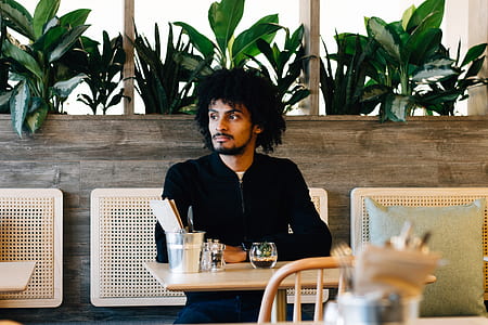 man wearing black zip-up jacket sitting near green leafed plant thumbnail