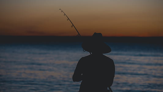 silhouette of person fishing on body of water at golden hour thumbnail
