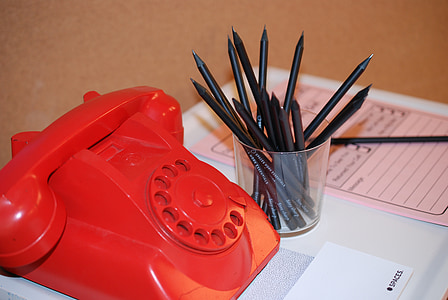 red rotary telephone beside clear glass pen organizedr thumbnail