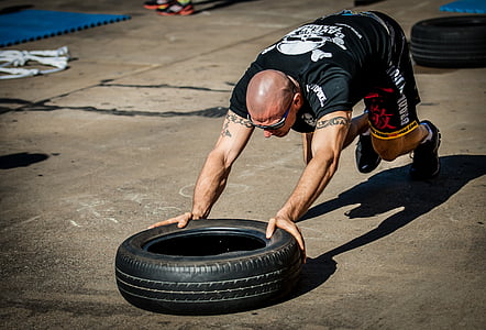 man in black shirt pushing tire on pavement during daytime thumbnail