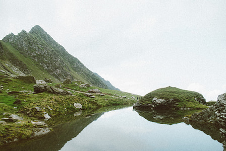 green grass field mountain beside body of water during daytime thumbnail
