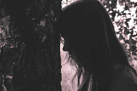 woman leans forehead on tree trunk in silhouette photo thumbnail