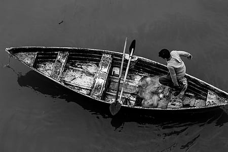 grayscale photo of man standing on canoe boat thumbnail