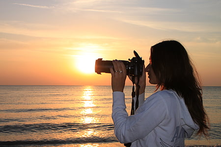 woman holding DSLR camera near beach during golden hour thumbnail