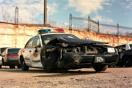 wrecked black and white police cruiser near other vehicles parked on lot at daytime thumbnail