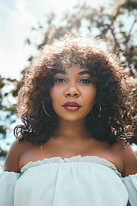 woman wearing white off-shoulder top standing beside tree during daytime thumbnail