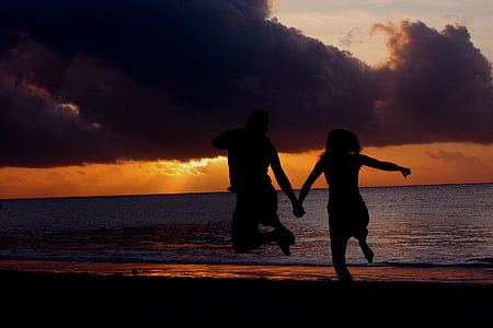 silhouette photo of two person's jumping in front of body of water thumbnail