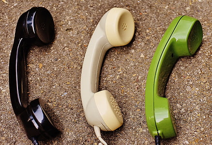three black, white, and green corded telephones on brown surface thumbnail