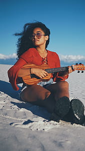 person sitting on sand while playing guitar thumbnail