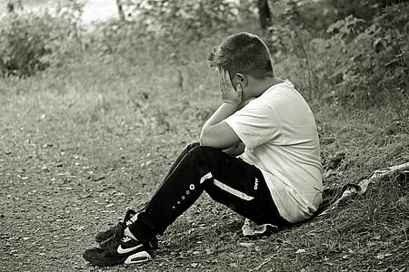grayscale photo of man holding face while sitting on grass field thumbnail