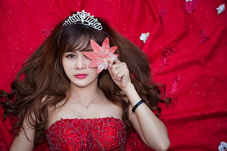 woman in red strapless sequined dress holding red petaled flower thumbnail