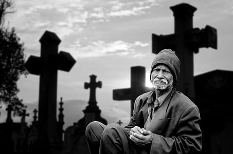 grayscale photo of a man sitting near black cross thumbnail