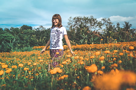 photo of woman in white crew-neck T-shirt walking on flower field during daytime thumbnail