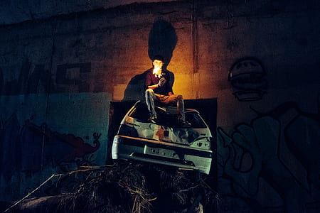 man sitting on top of white abandoned car near wall thumbnail