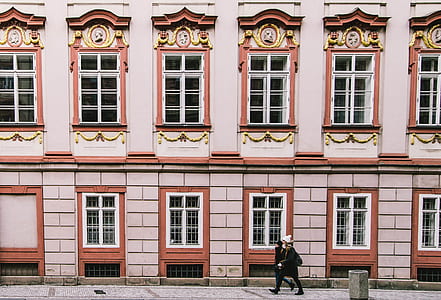 two persons walks beside beige and white concrete building during daytime thumbnail