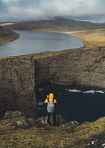person on edge of a cliff near body of water during cloudy day thumbnail