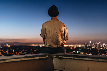 person sitting on fence looking to city buildings during nighttime thumbnail